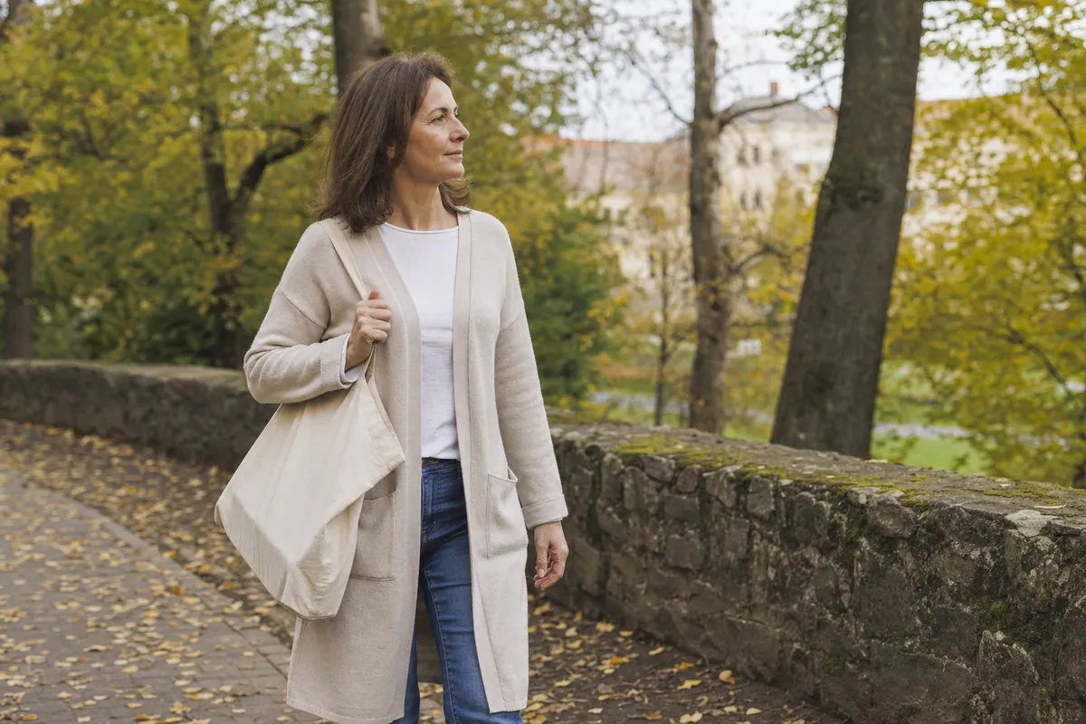 Žena jde podzimním parkem s plátěnou taškou
